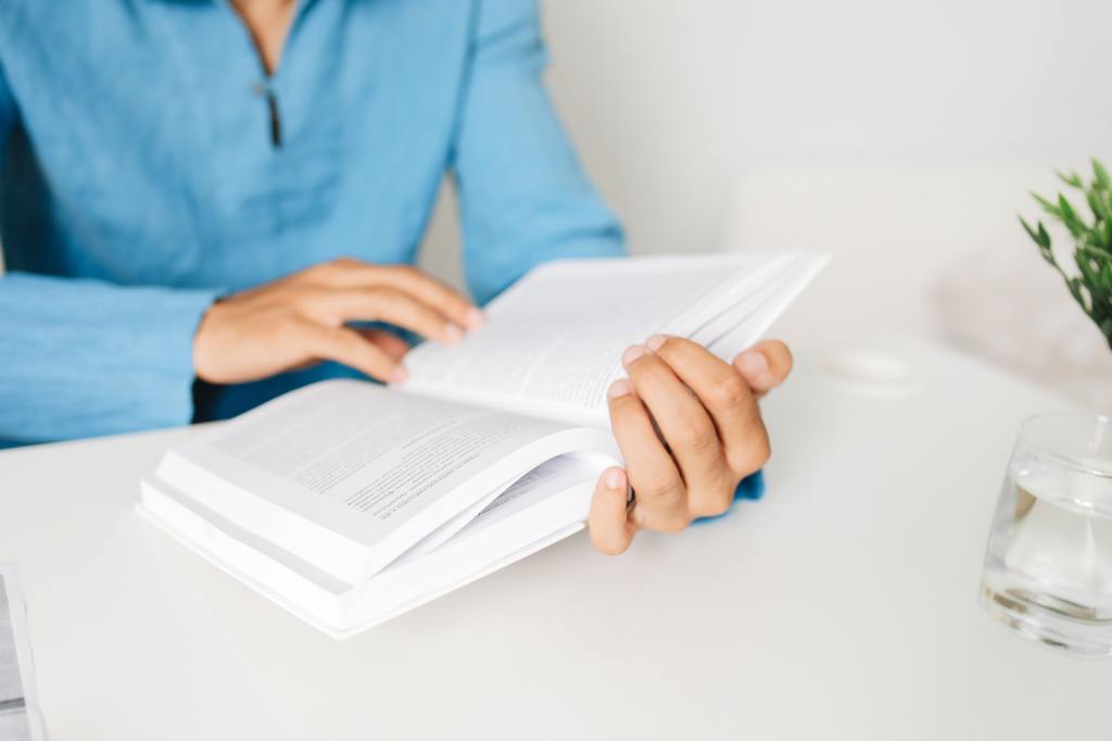 Person in a blue shirt reading a book on a white table